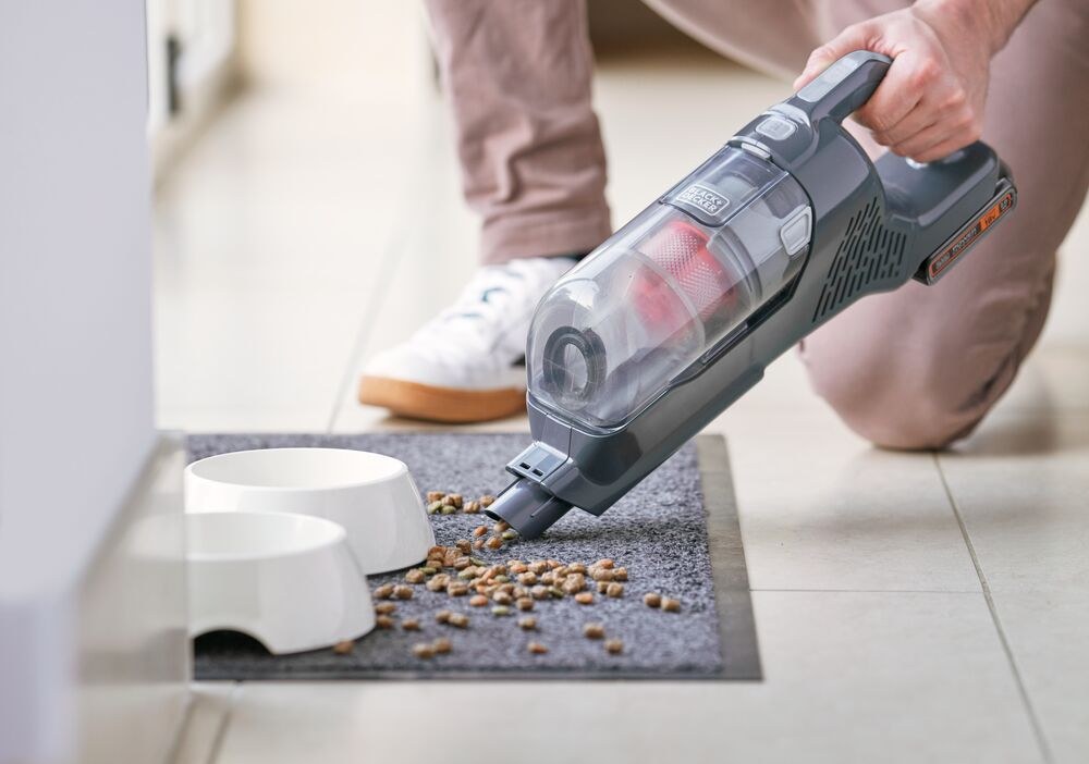 Η BLACK+DECKER σε λειτουργία σκούπας χειρός μαζεύει τροφή κατοικιδίου από πατάκι δίπλα σε μπολ